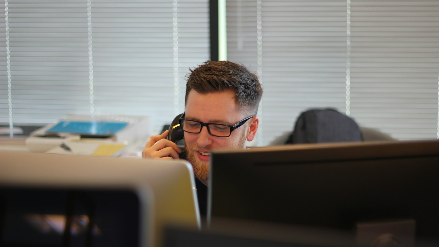 A male dispatcher speaking on the phone while sitting at a desk with computers.
