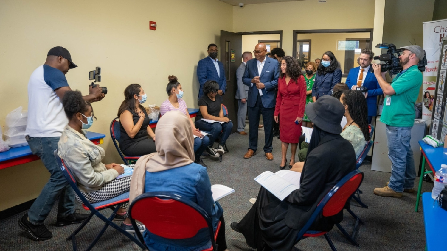 The header image depicts a significant moment captured during the approval of the "Harris County Commissioners Approve First of its Kind Community-led Multi-million Dollar Youth Justice Community Reinvestment Fund" article. The photo showcases a diverse group of community members and youth gathered in a room. The atmosphere is filled with joy and celebration, evident from the smiling faces and engaged body language of the individuals present. Some individuals are wearing face coverings and masks, indicating the event happening during COVID-19 (2021). The occasion has attracted the attention of multiple press members, who can be seen documenting the event. This image captures the spirit of collaboration and community involvement in the approval of the groundbreaking reinvestment fund, which will re-envision public safety for youth in Harris County by investing in community programs that keep youth from becoming involved in crime and prevent youth incarceration.