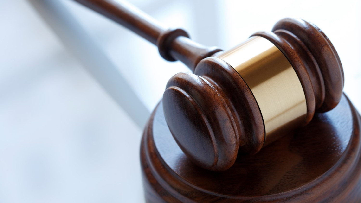The image shows a close up of a gavel resting on a sound block on top of a smooth white surface.