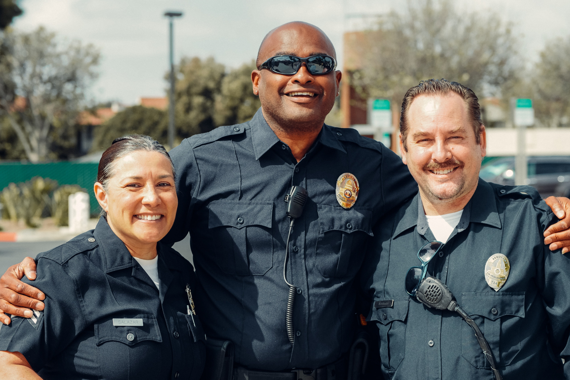 The photo features three law enforcement authorities standing together and smiling for a photo outside. Their body language exudes a sense of support, unity, and encouragement. They are positioned side by side with their expressions conveying an enthusiasm for their role in helping others. This positive image showcases the dedication and approachability of law enforcement authorities as they strive to provide assistance and support to the community.