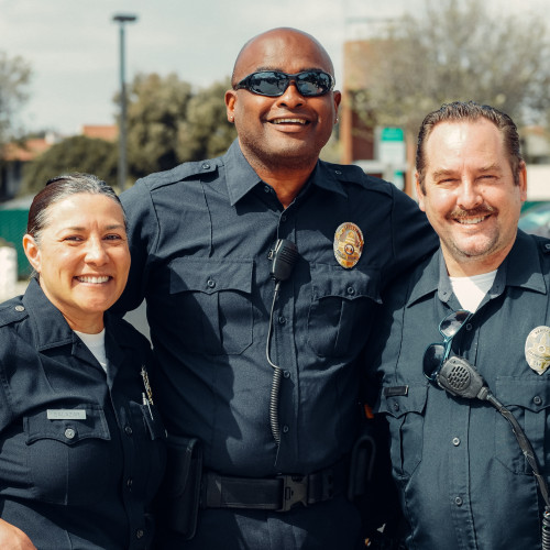 The photo features three law enforcement authorities standing together and smiling for a photo outside. Their body language exudes a sense of support, unity, and encouragement. They are positioned side by side with their expressions conveying an enthusiasm for their role in helping others. This positive image showcases the dedication and approachability of law enforcement authorities as they strive to provide assistance and support to the community.